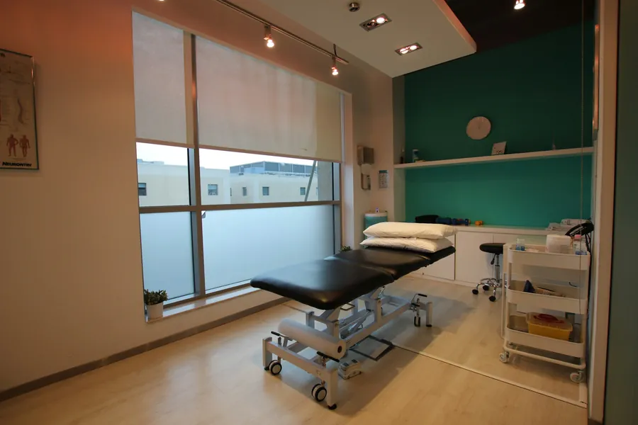 Una stanza di fisioterapia con il lettino, la parete verde e la finestra grande
