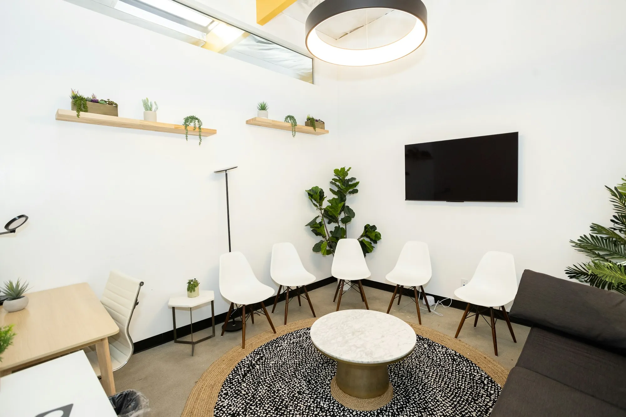 Una sala d'attesa luminosa, con sedie bianche, piante e un tappeto rotondo